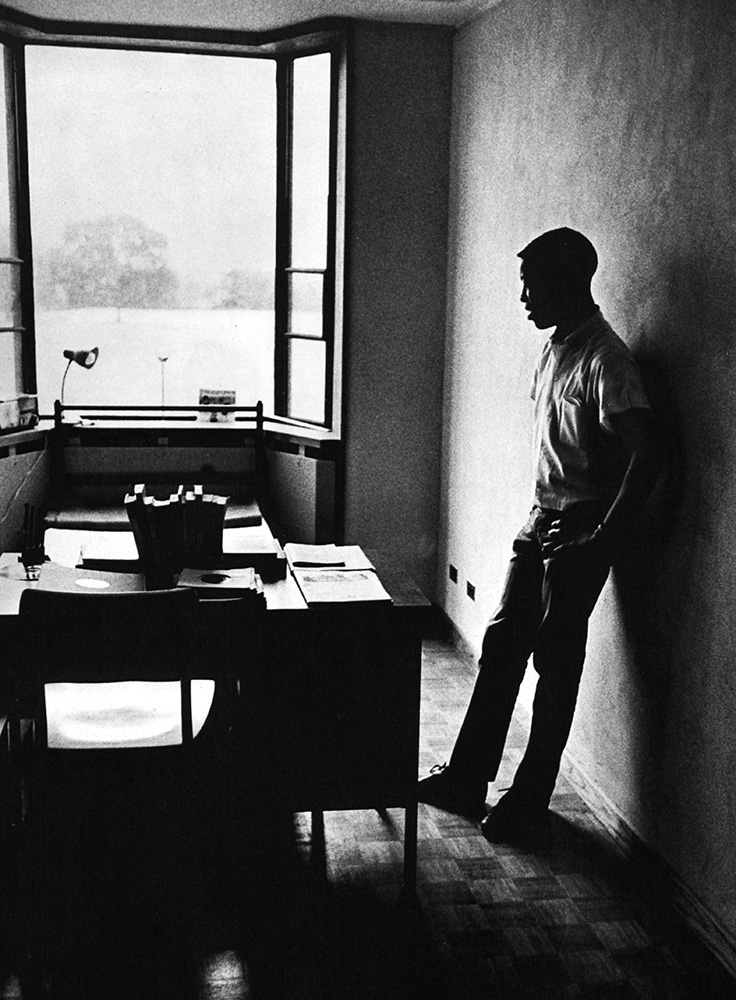 A student participant in the Princeton College Summer Program takes a study break, He is leaning against a wall next to his desk, circa 1960. The program was designed to improve Black education through individual experiences.