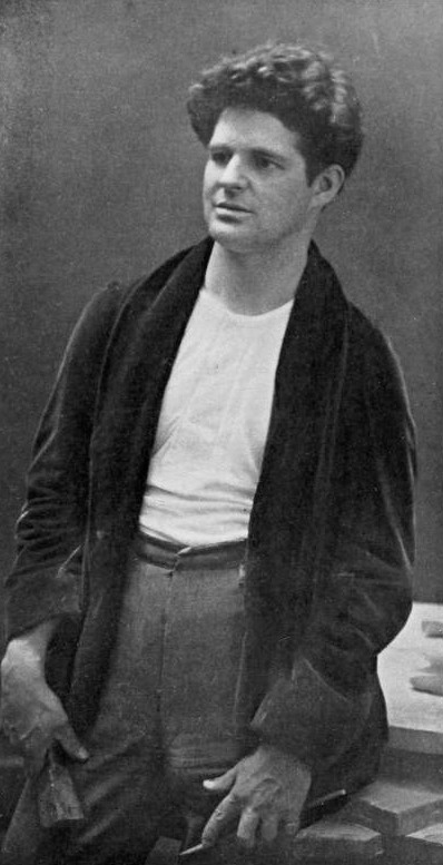 A portrait of George Grey Barnard, dressed in a tee-shirt and dark cardigan, in his studio.