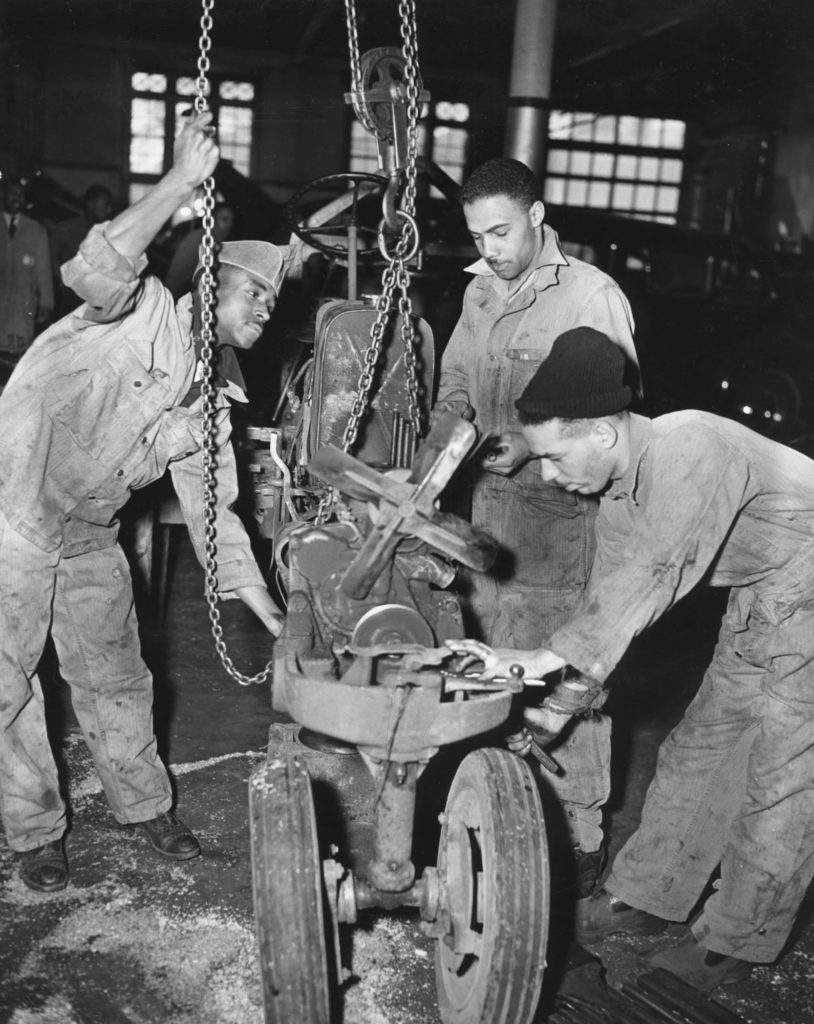 Three black students work on a machine as part of the department of auto diesel mechanics at the Hampton Institute. 