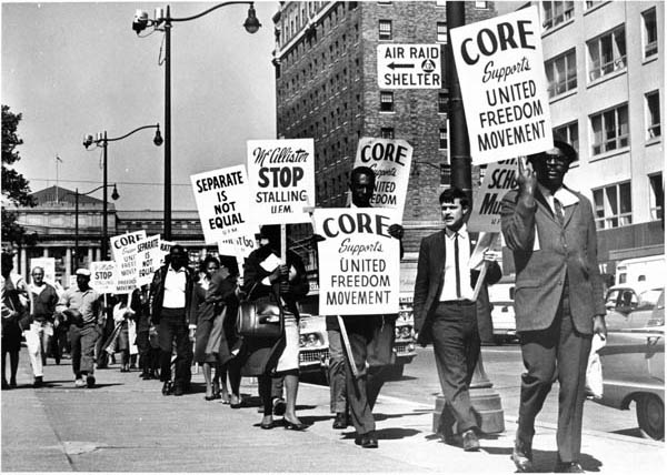 Black and white men and women in formal dress march in a picket line, with signs reading "CORE Supports United Freedom Movement." 